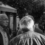 Foto em preto e branco de cinco idosos conversando em uma praça