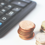 Parte de calculadora próxima a três pilhas de moedas